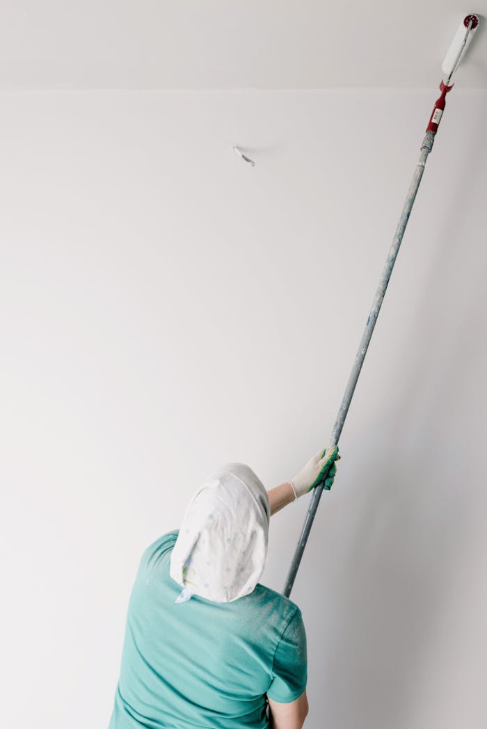 why-choose-us Back view of anonymous male worker with roller painting ceiling while working at home